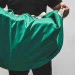 Osoba trzymająca duży zielony worek transportowy przeznaczony do przewozu odzieży i tekstyliów w zakładach pralniczych RTP Radom.