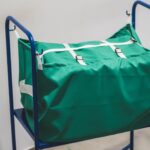 Metalowy wózek transportowy RTP Radom z zielonym workiem tekstylnym zabezpieczonym białymi paskami z klamrami, używany w profesjonalnej logistyce pralniczej.
